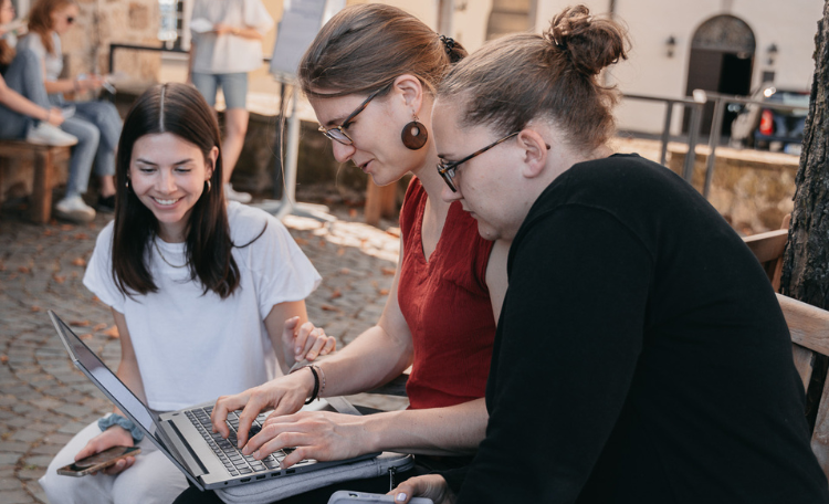 Drei Chatbegleiterinnen sitzen um einen Laptop